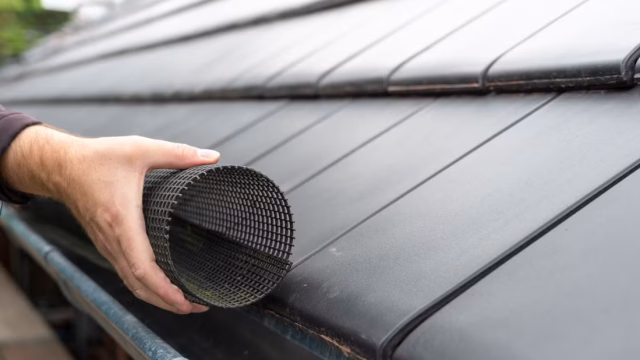 hand-installing-a-gutter-guard-mesh-over-a-gutter-on-the-side-of-a-roof